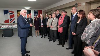 Bundesminister des Auswärtigen Frank-Walter Steinemeier steht vor den Mitarbeiter und Mitarbeiterinnen des Politischen Archivs und bedankt sich. Im Hintergrund hängen Ausschnitte der Fahnen der Länder, die den 2+4 Vertrag unterzeichnet haben an der Wand.