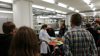 Gäste zu Besuch in der Restaurierungswerkstatt, wo eine zerstörte Akte gezeigt wird.